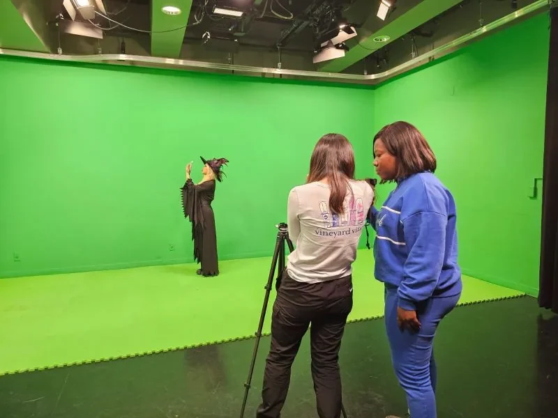 Behind the scenes on the green screen stage: the actor in costume with a wand while the crew films